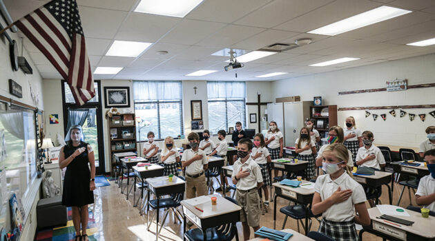 Fourth-grade teacher Kristina Tons, wearing a clear plastic face shield, leads her class in the Pledge of Allegiance.