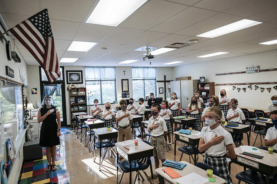 Fourth-grade teacher Kristina Tons, wearing a clear plastic face shield, leads her class in the Pledge of Allegiance.