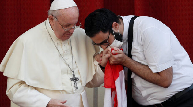 A masked Maronite Father Georges Briedi kisses the hand of Pope Francis