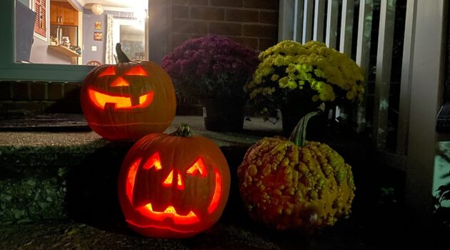 Carved jack-o-lanterns glow at night on the porch steps of a house
