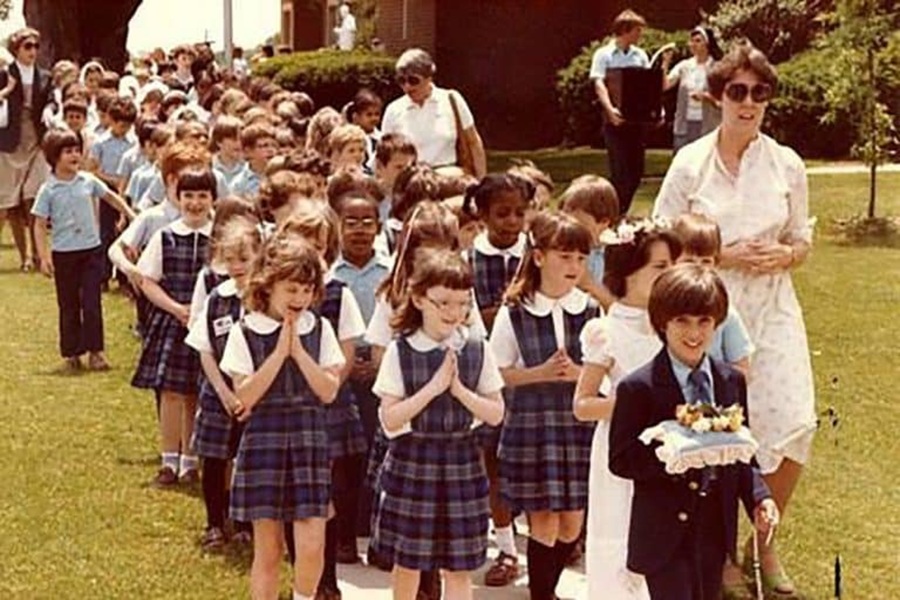 Children in school uniforms walk together with hands folded in a May Procession to honor the Blessed Mother