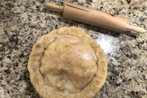 A homemade pie that is ready to bake sits on a kitchen counter next to a rolling pie