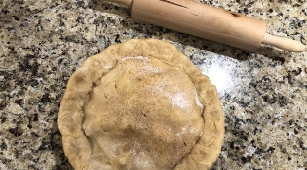 A homemade pie that is ready to bake sits on a kitchen counter next to a rolling pie