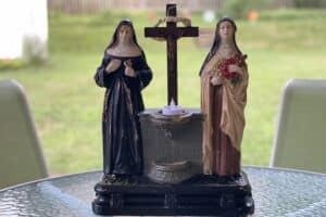Sculpture of St. Rita and St. Therese with a cross and holy water font at the center sits on a table