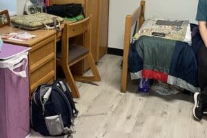 A college dorm room with a backpack, desk, part of a bed