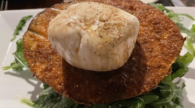 Caprese salad on a plate with a ball of mozzarella on a piece of fried eggplant atop greens