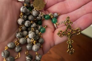 A hand holds a Rosary with a crucifix prominently displayed