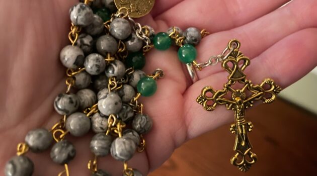 A hand holds a Rosary with a crucifix prominently displayed