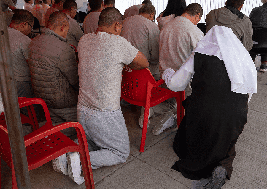 Sister Elaine Elgart, a member of the Eudist Servants of the 11th Hour, kneels withs inmates during Mass