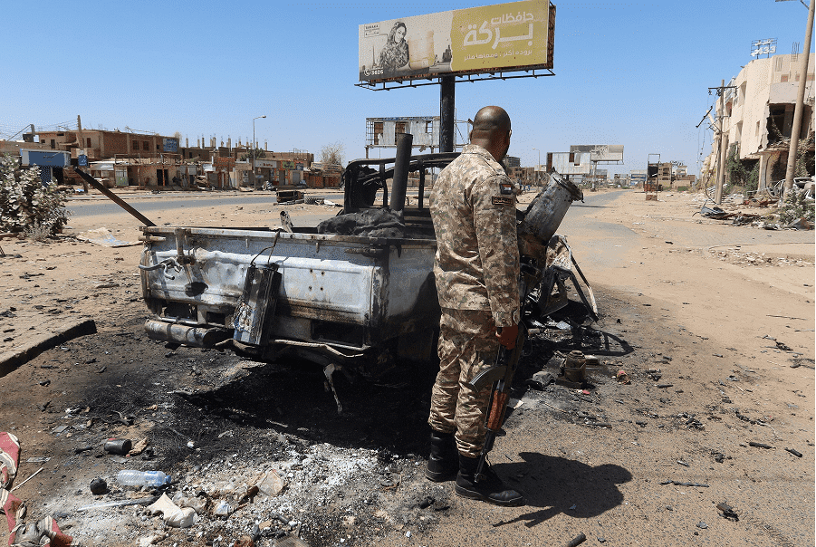 A Sudanese army soldier stands next to a destroyed combat vehicle