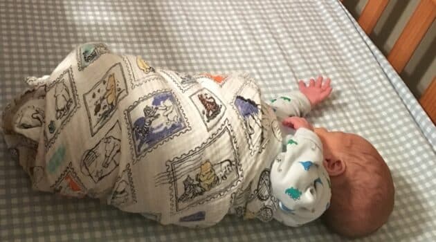 Baby wrapped in a blanket lies in crib