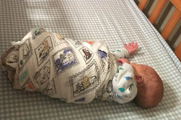 Baby wrapped in a blanket lies in crib