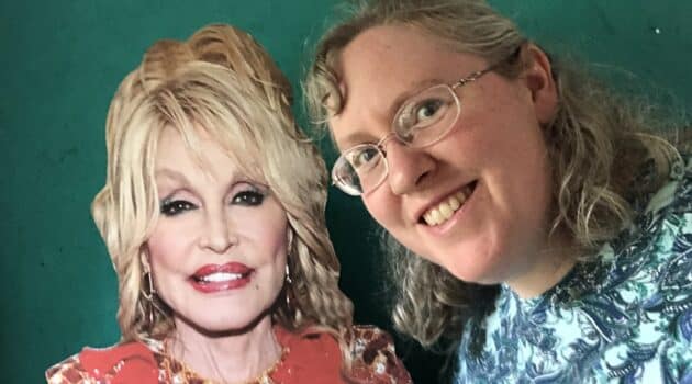 The writer poses with a cardboard cutout of Dolly Parton against a green background