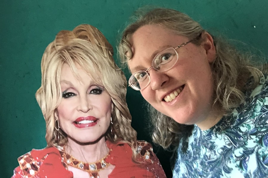 The writer poses with a cardboard cutout of Dolly Parton against a green background