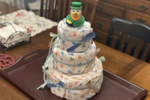 A tower of diapers with baby toys tied on and a rubber duck on top