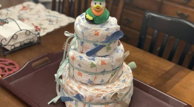 A tower of diapers with baby toys tied on and a rubber duck on top