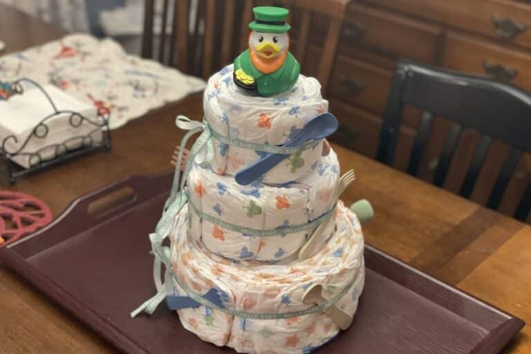 A tower of diapers with baby toys tied on and a rubber duck on top