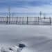 A snowy field with a fence under a blue sky