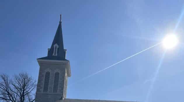 Church steeple against a blue sky with the shining sun