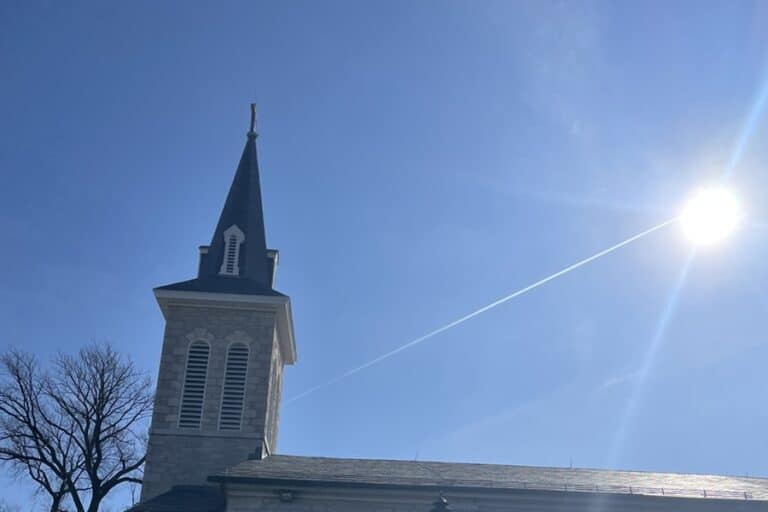 Church steeple against a blue sky with the shining sun