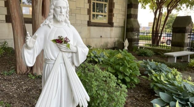 White statue of Jesus stands in a garden outside a church