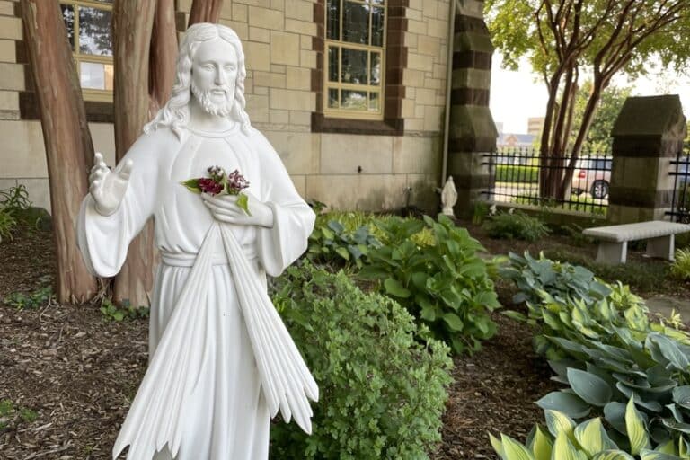 White statue of Jesus stands in a garden outside a church