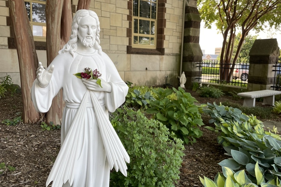 White statue of Jesus stands in a garden outside a church