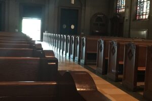 Pews in a church with sunlight streaming through the main door at the center