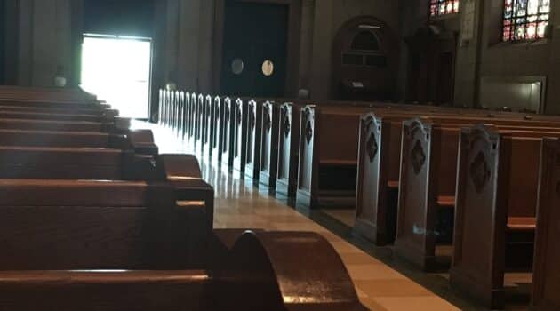 Pews in a church with sunlight streaming through the main door at the center